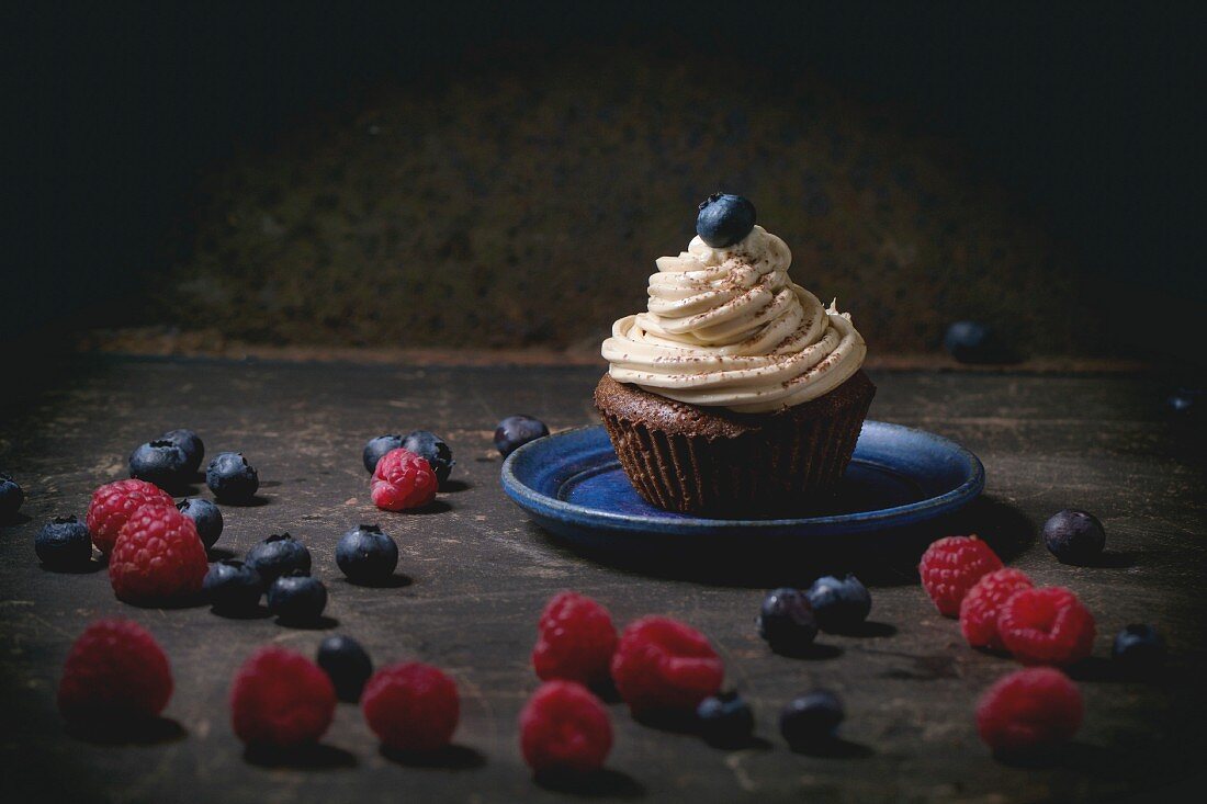 Chocolate cupcake with butter coffee cream and fresh berries over dark background