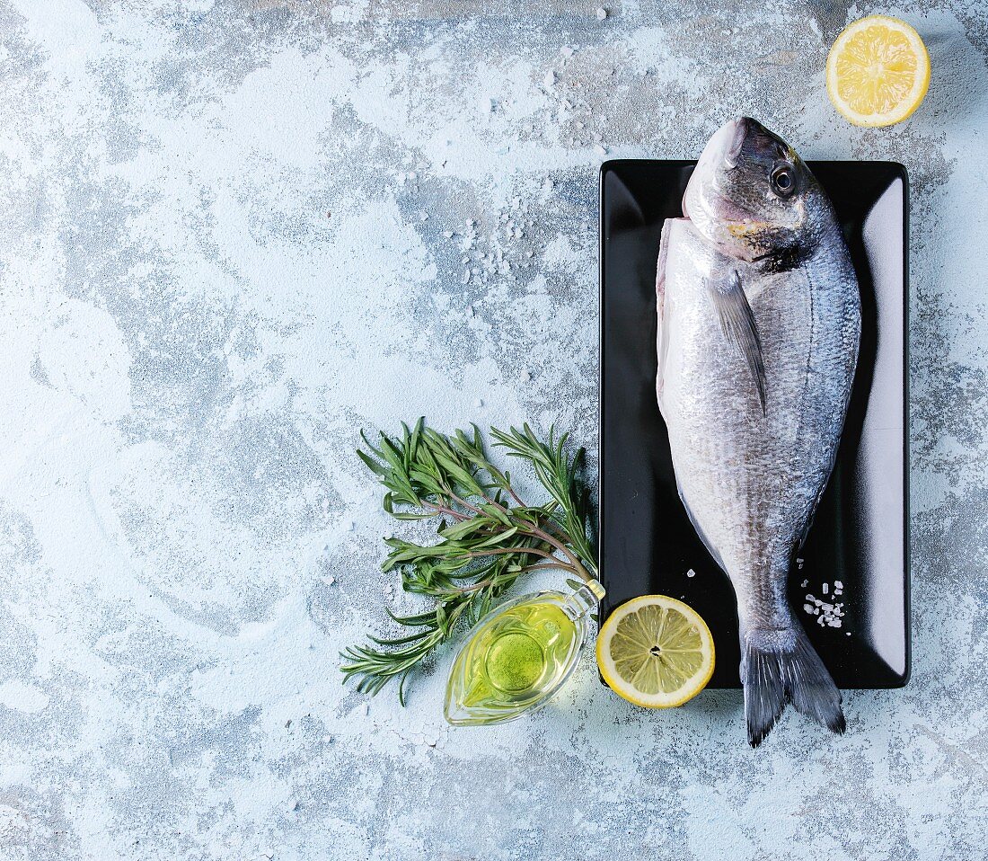 Raw bream fish with herbs, lemon and olive oil over blue textured background