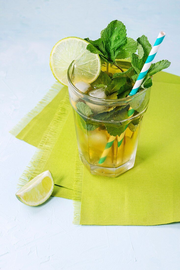 Glass of Iced green tea with lime, lemon, mint and ice cubes on green textile napkin