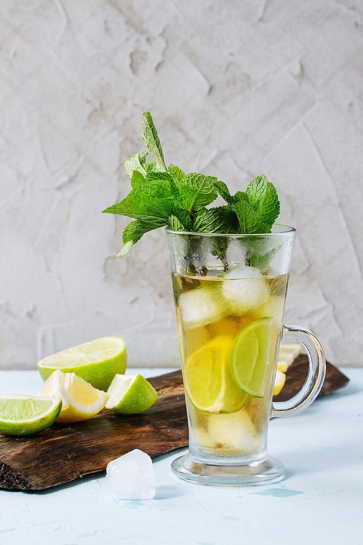 Glass of Iced green tea with lime, lemon, mint and ice cubes on wooden chopping board