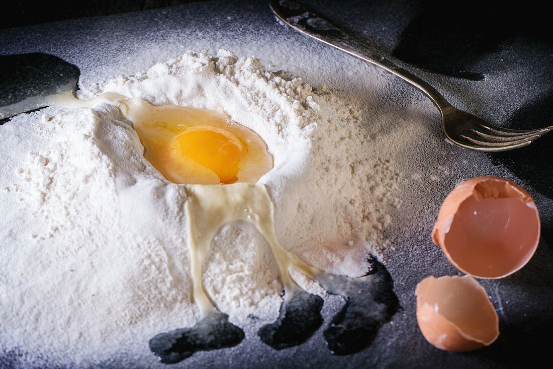Ingredients for dough making. Sifted flour and brocken egg on black slate board