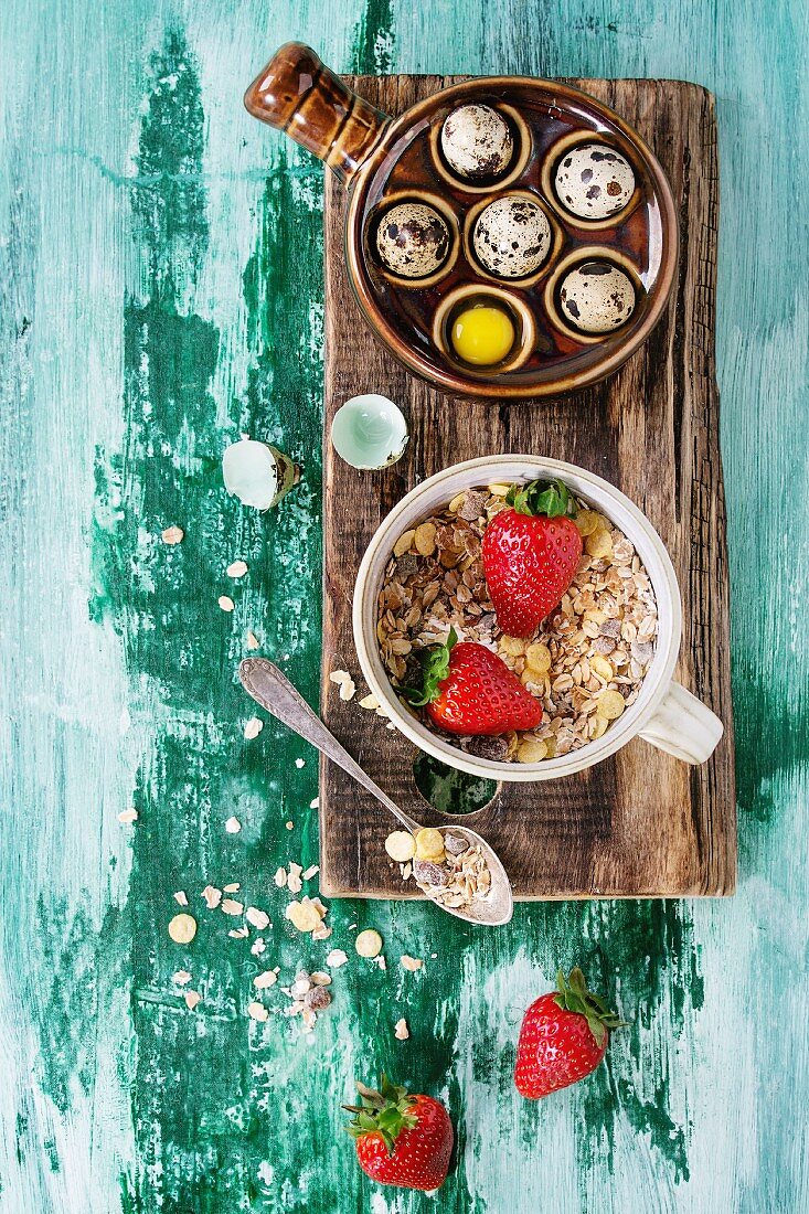 Ingredients for healthy breakfast. Quail eggs, bowl of muesli and strawberries on wood chopping board