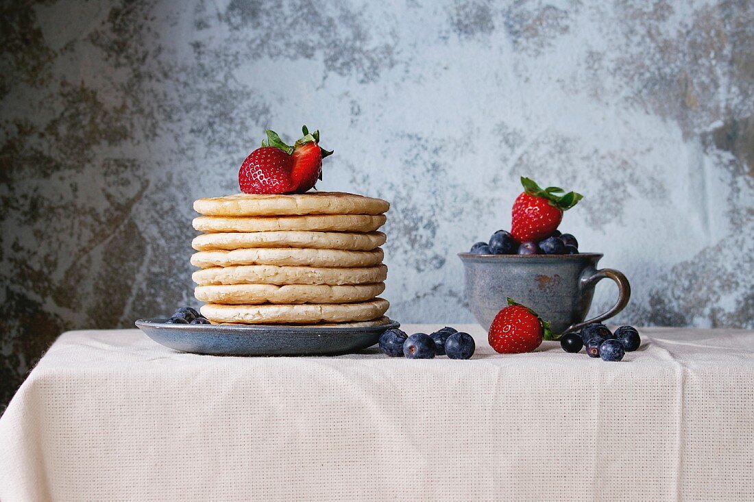 Breakfast with Pancakes with fresh strawberries and blueberries served on white linen tablecloth