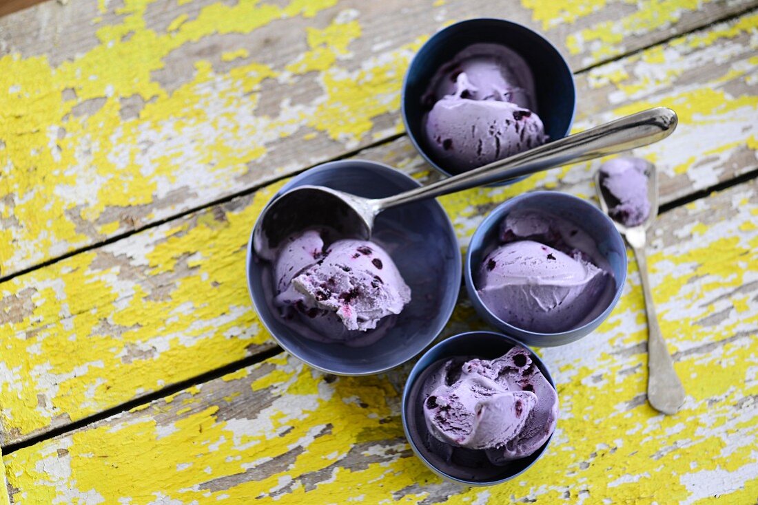 Several bowls of blueberry ice cream on a wooden background