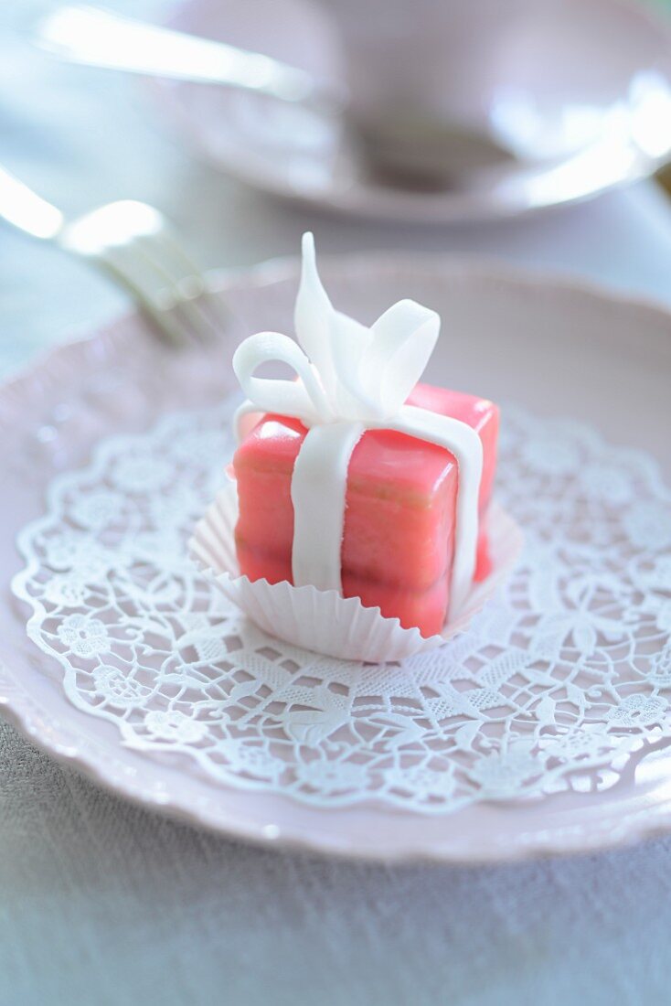 A pink petit four on a paper doily
