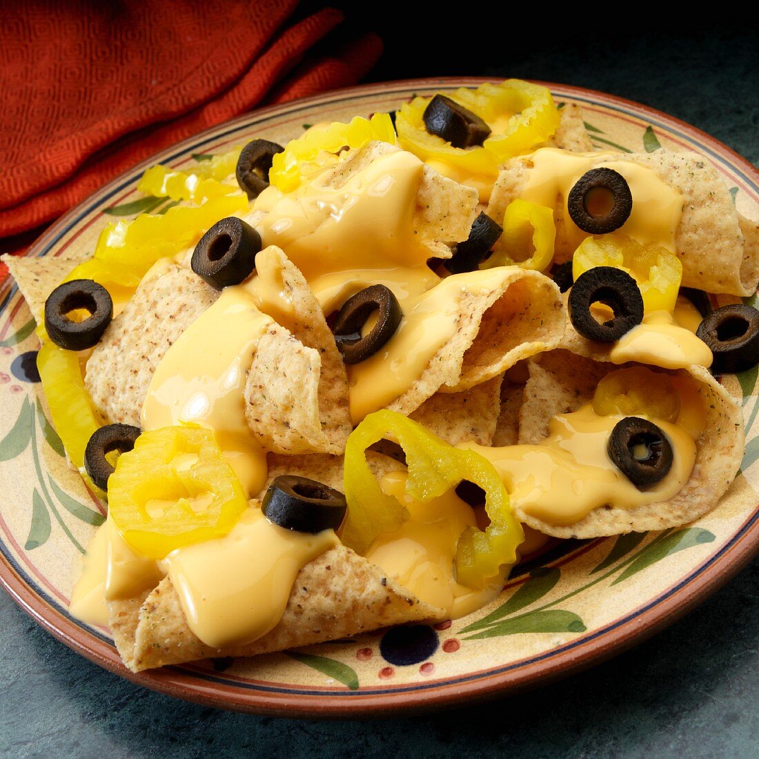 Tortillachips mit Käsesauce, schwarzen Oliven und Peperoni