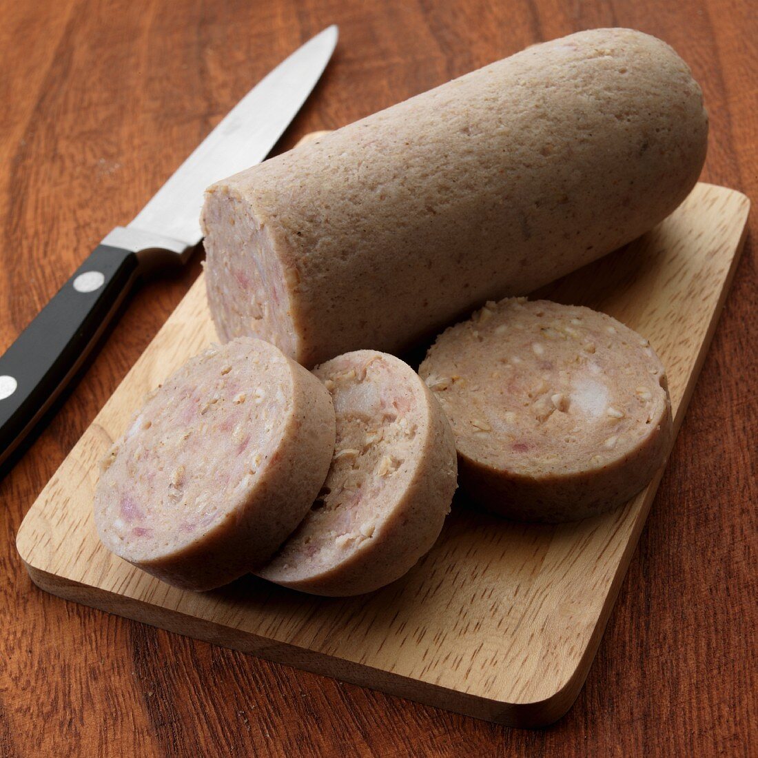 Uncooked English white pudding on cutting board with knife