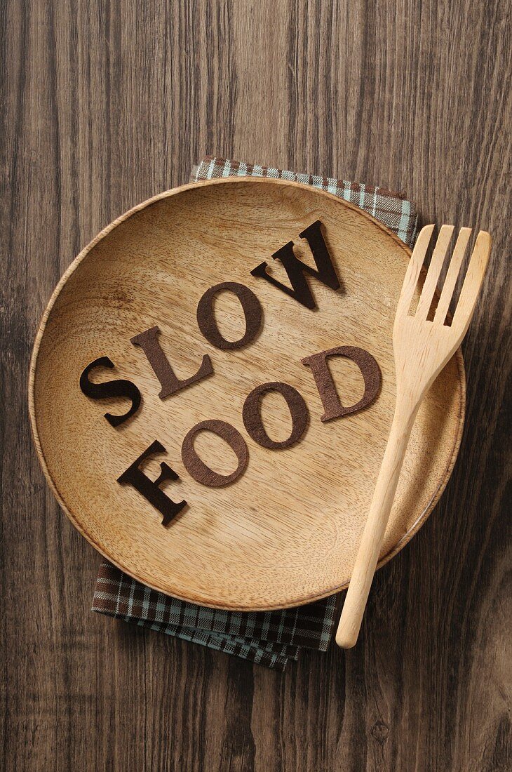 Schrift Slow Food auf Holzteller mit Gabel