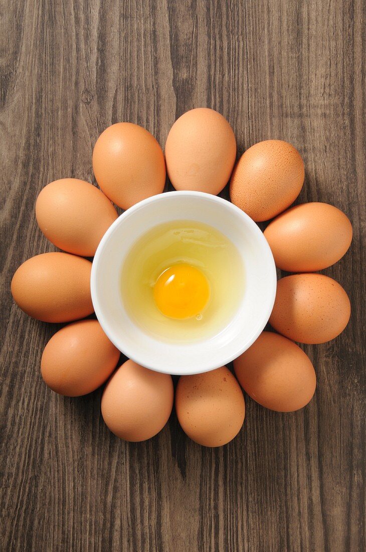 An egg yolk in a bowl surrounded by whole eggs