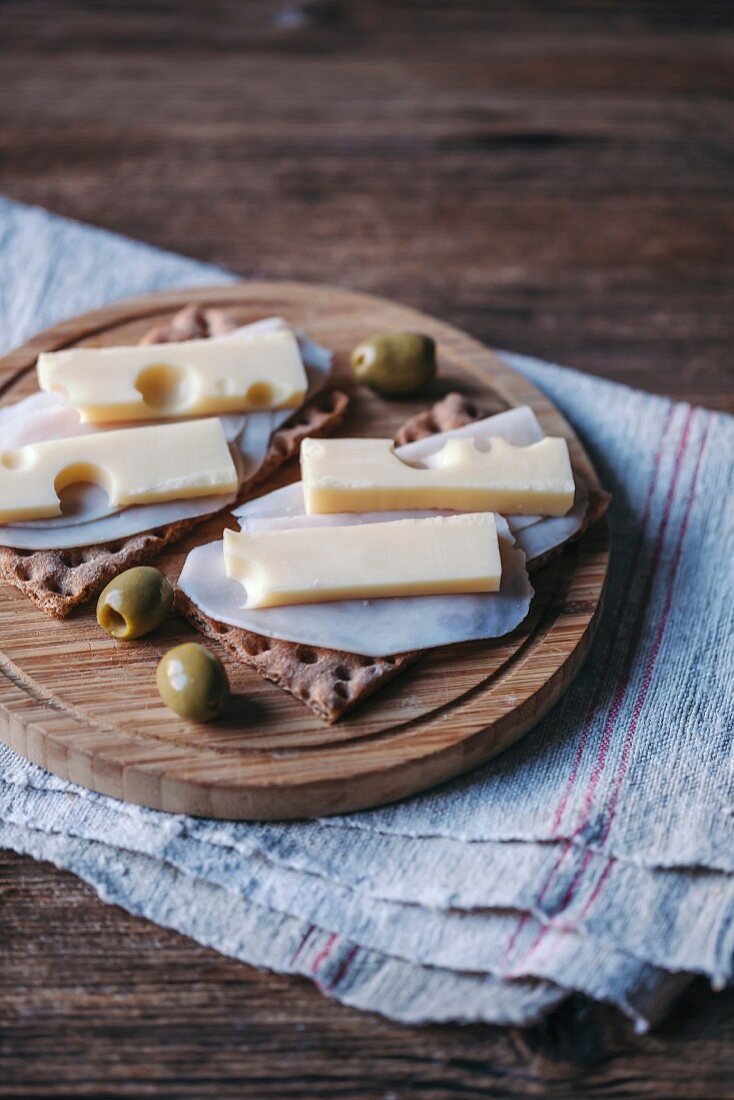 Knäckebrot belegt mit Schinken und Käse serviert mit Oliven auf Holzbrett