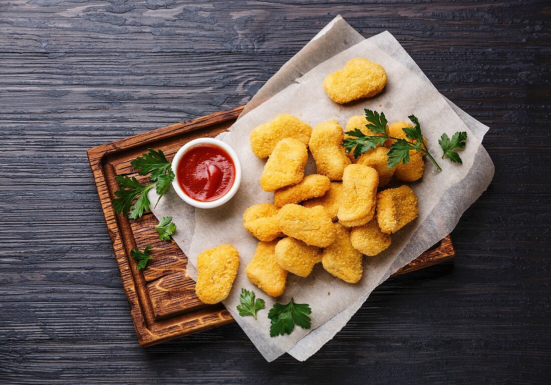 Chicken nuggets and ketchup sauce on black burned wooden background copy space