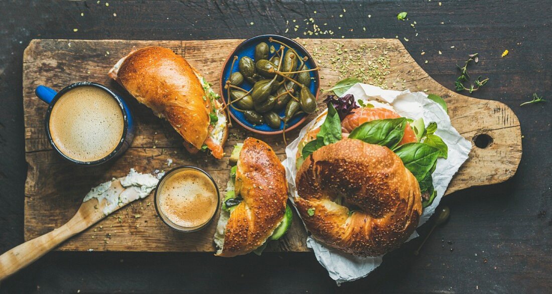 Frühstücksbagel belegt mit Lachs, Avocado, Frischkäse und Basilikum, dazu Kaffee