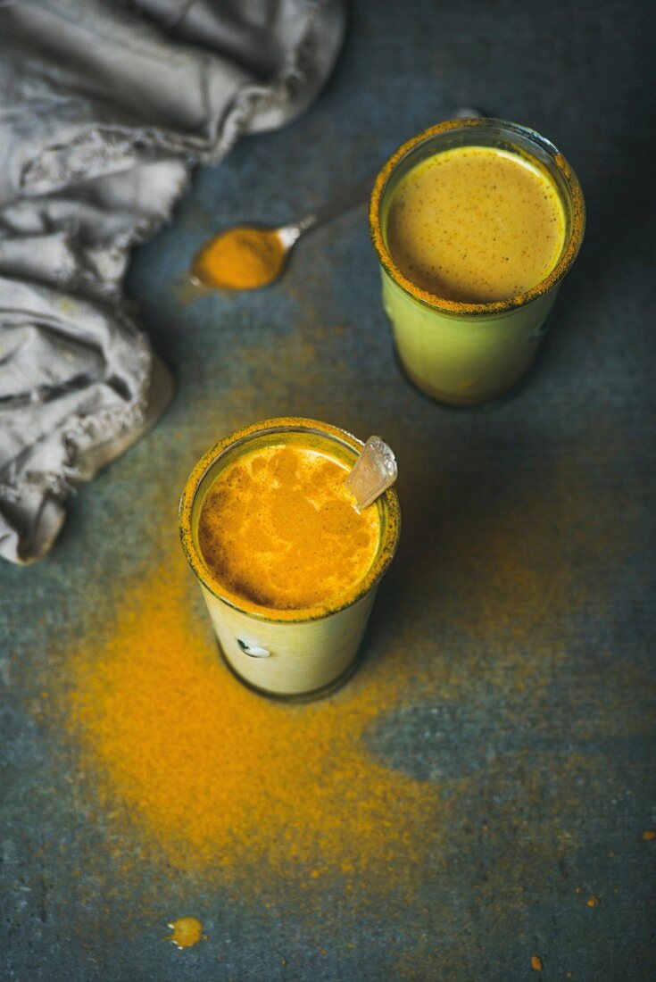 Golden milk with turmeric powder in glasses over dark grunge background