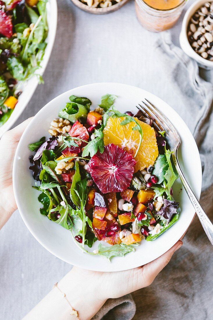 A woman is holding a large plate of Citrusy Roasted Beet Goat Cheese Salad with Black Eyed Peas