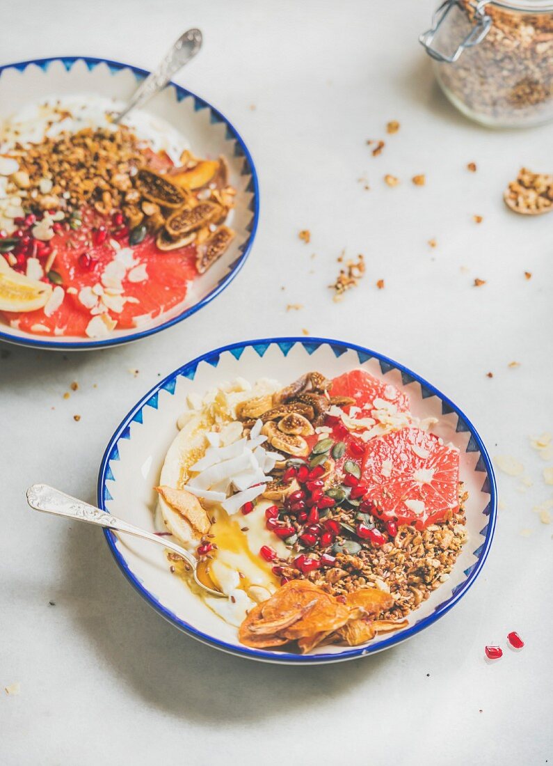 Healthy breakfast yogurt bowls with granola, grapefruit, banana, pomegranate, dried fruit, nuts and seeds