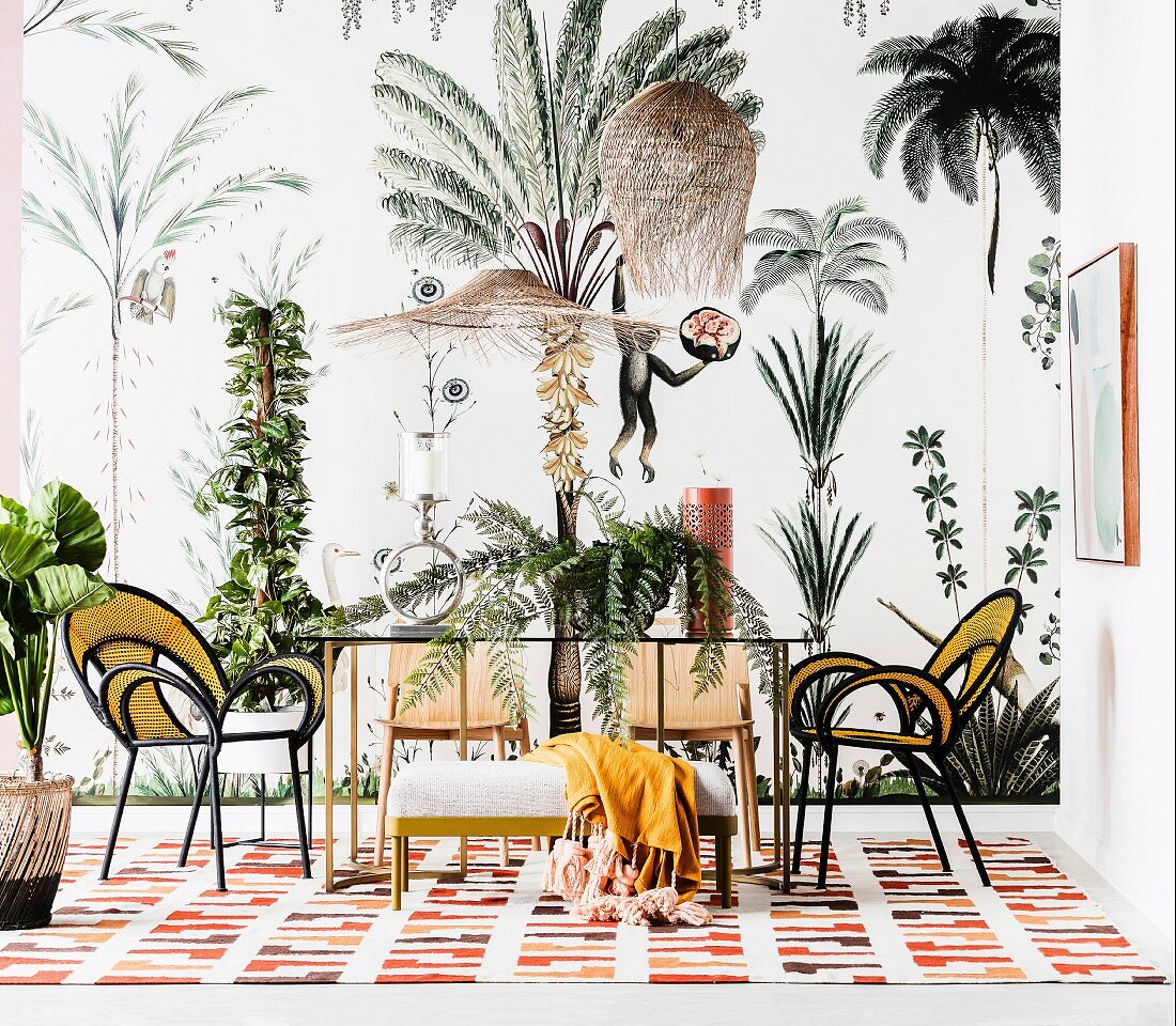 Dining table with glass top and designer chairs in front of wallpaper with plant and animal motifs