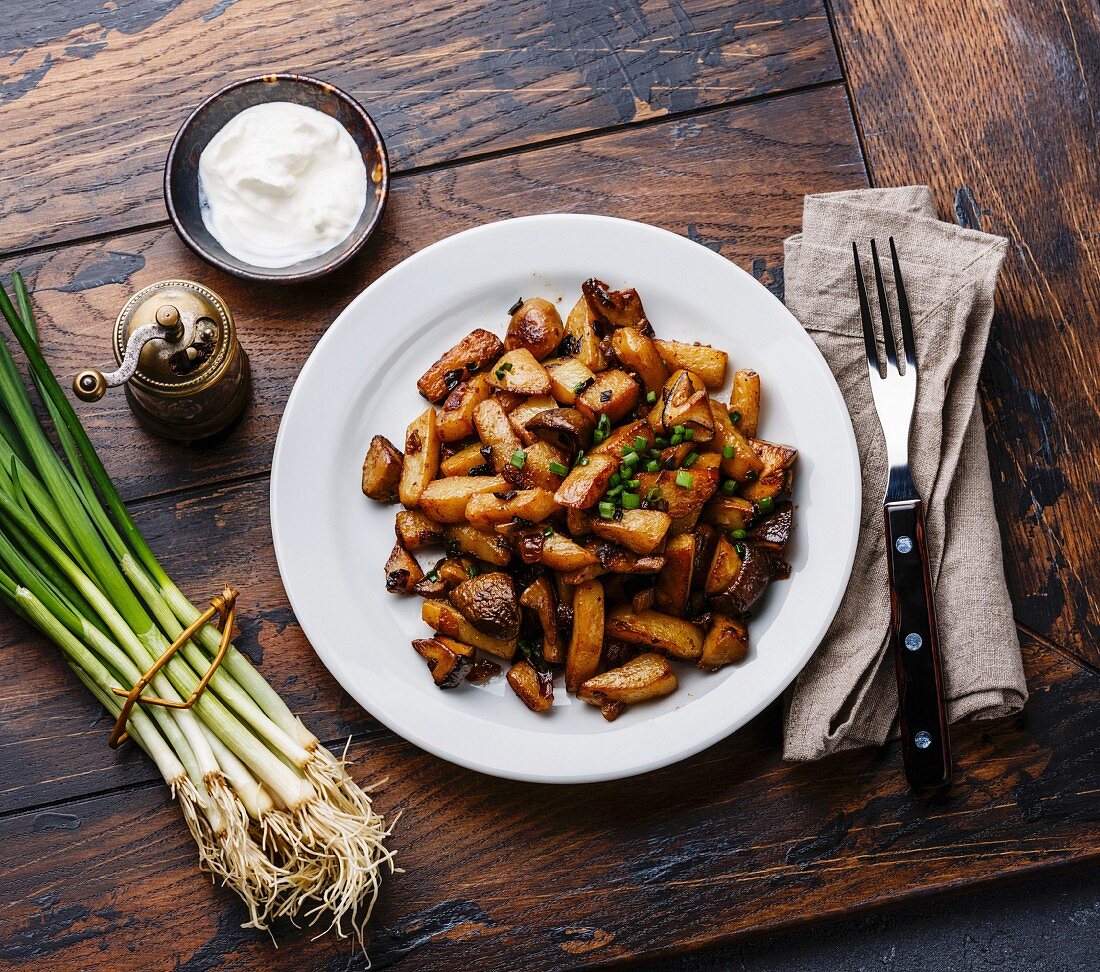Fried potatoes roasted with Porcini wild mushrooms on white plate and green onions on wooden table background