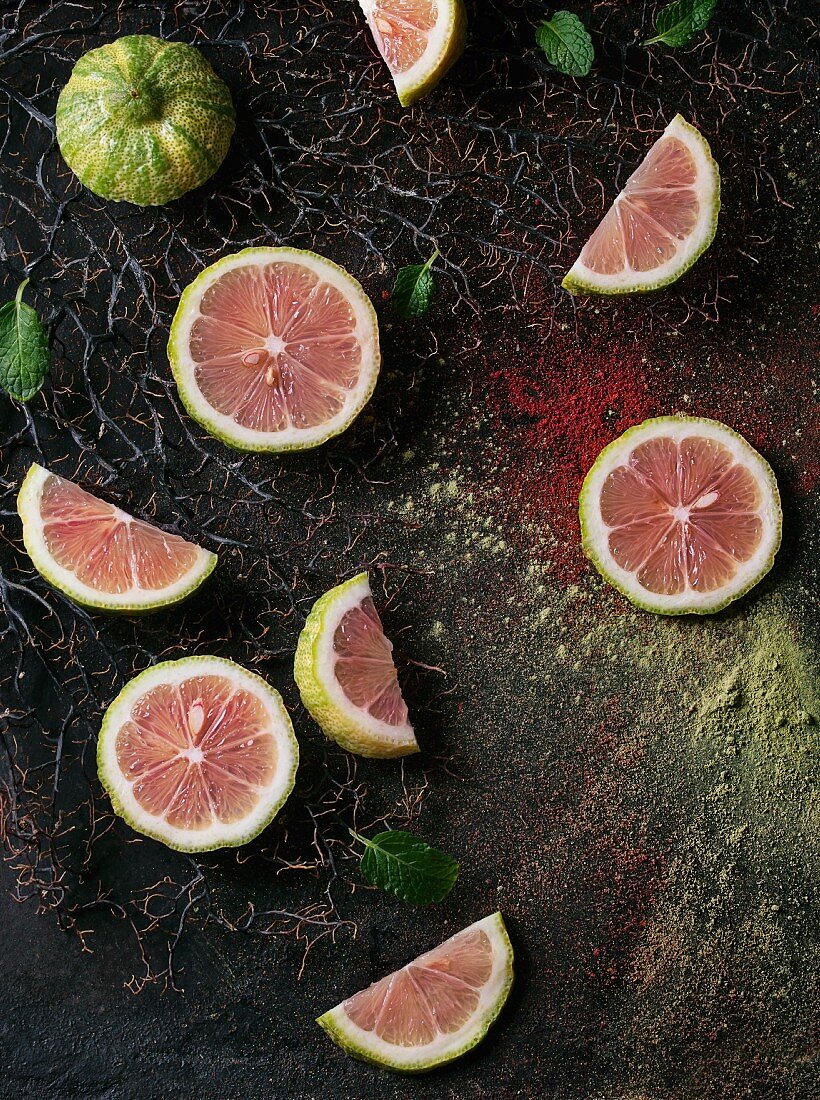 Sliced pink tiger lemon with mint leaves on branches with pink and green powder