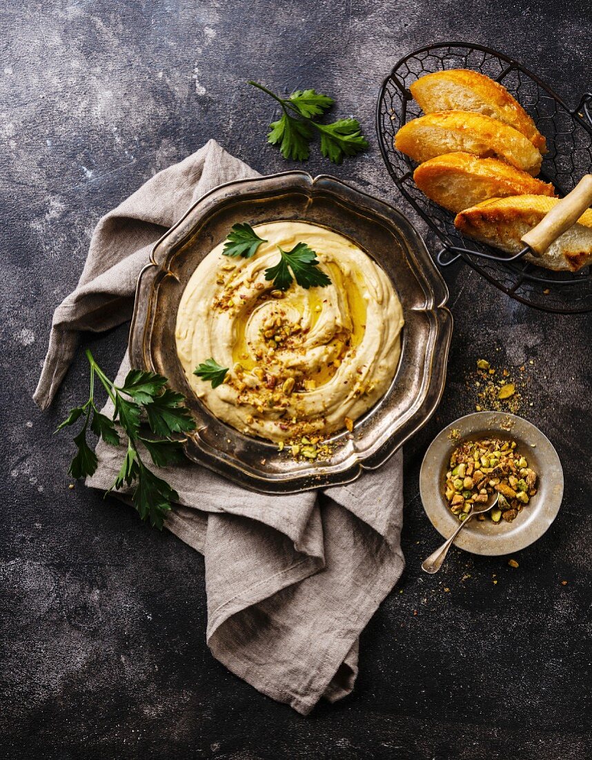 Homemade hummus with pistachios and bread toasts in metal plate on black stone background