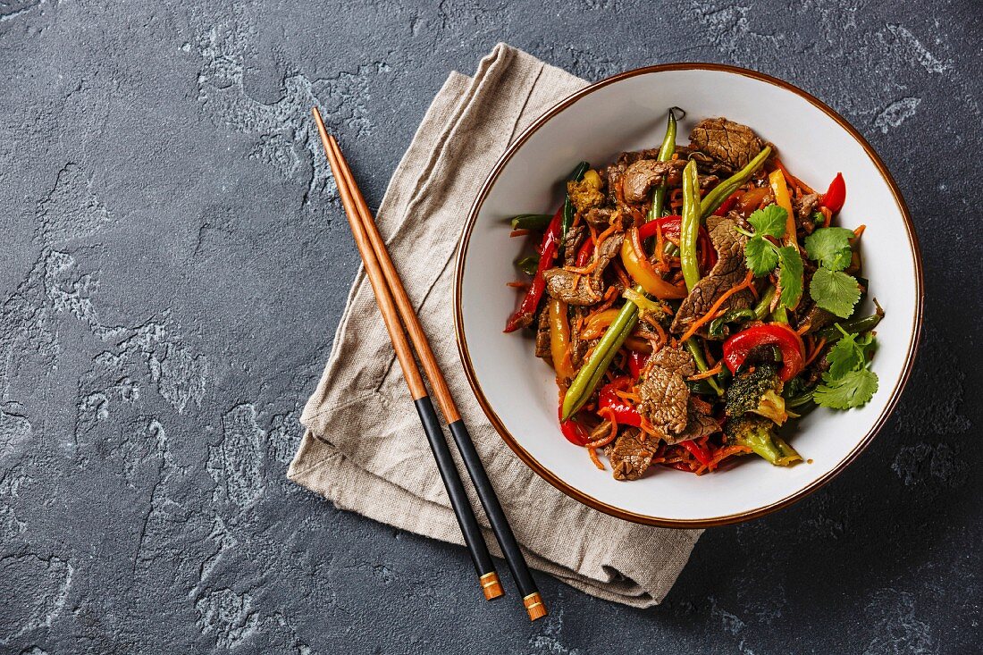 Stir fry beef with vegetables in bowl on dark stone background