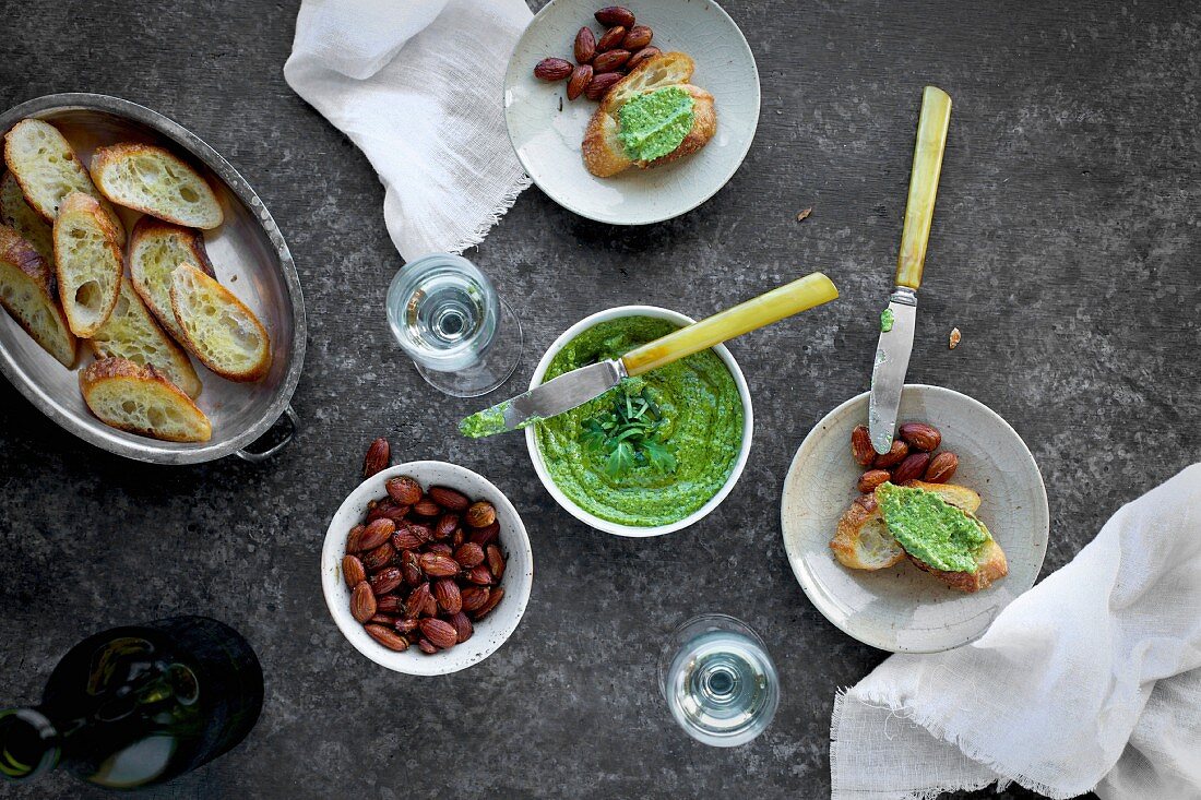 Arugula Chive Basil Pesto served in a ceramic bowl with crostini, almonds and wine