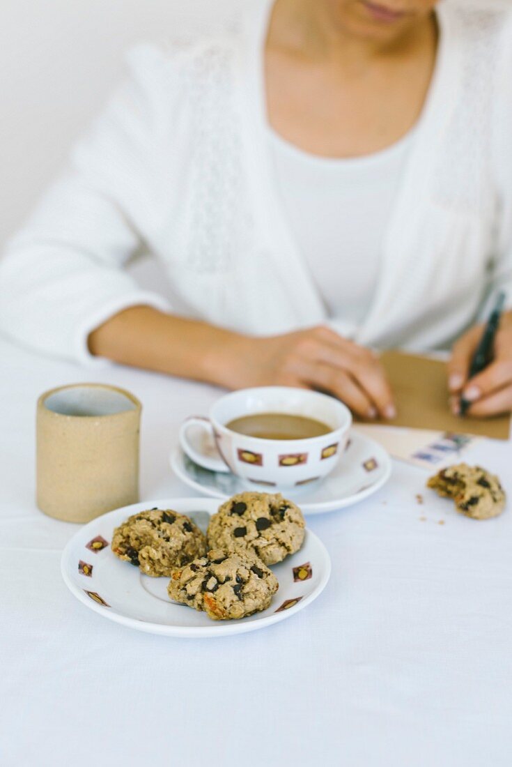 Frau schreibet Brief an edecktm Tisch mit Chocolate Chips Cookies und Kaffeetasse
