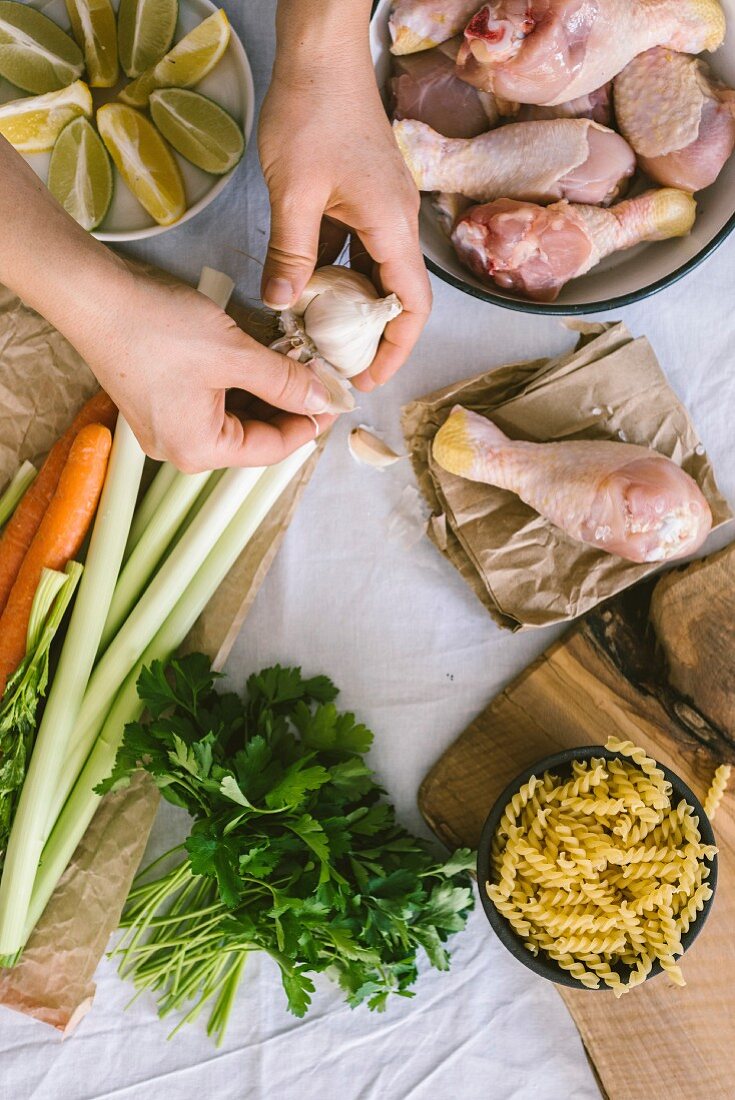 Hands preparing the ingredients for chicken soup with pasta, leek and carrot