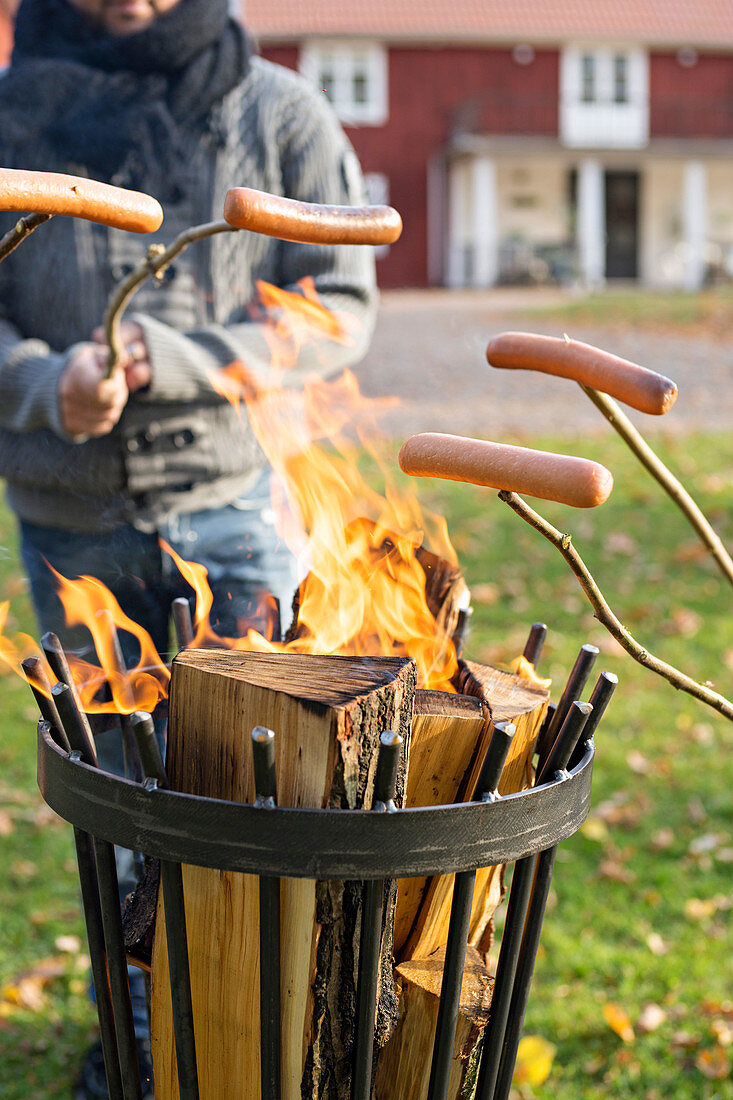 Würste an Stöcken werden am Feuer im Feuerkorb gegrillt