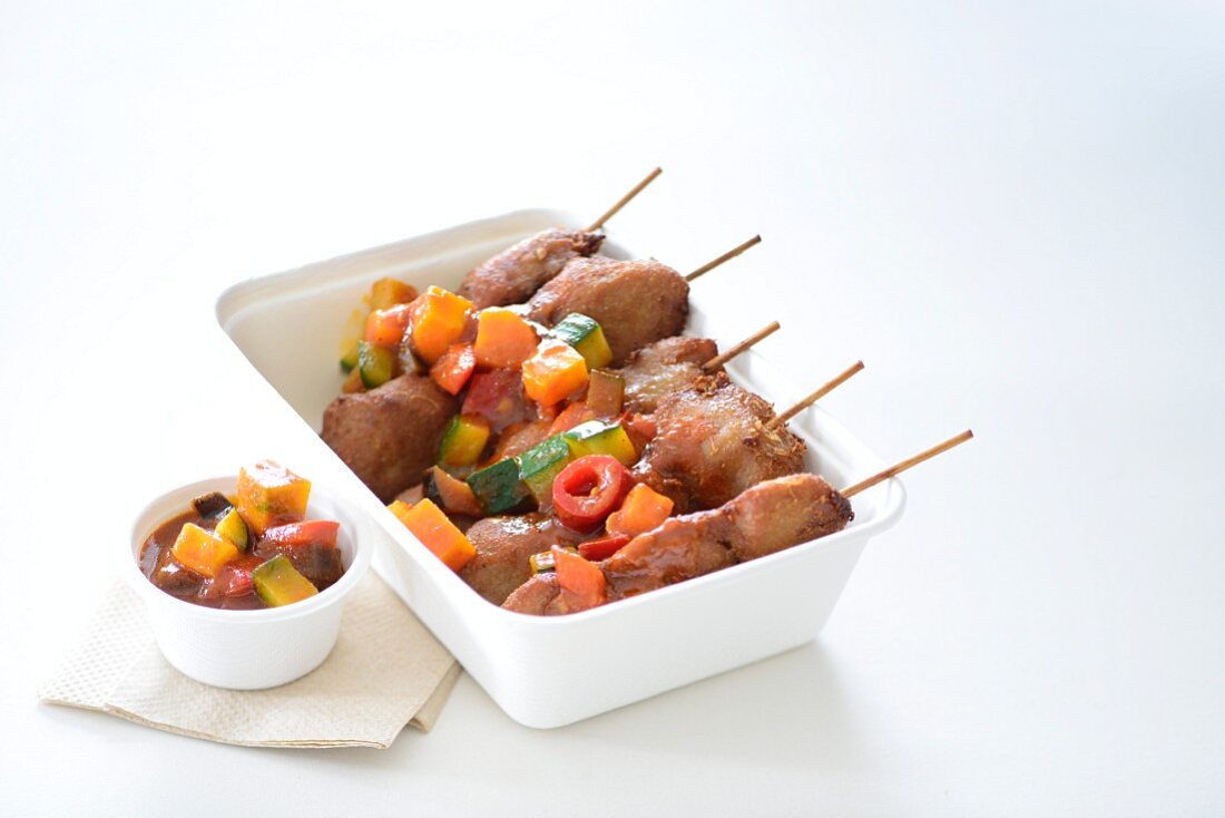 Pork skewers with vegetable sauce in a takeaway box