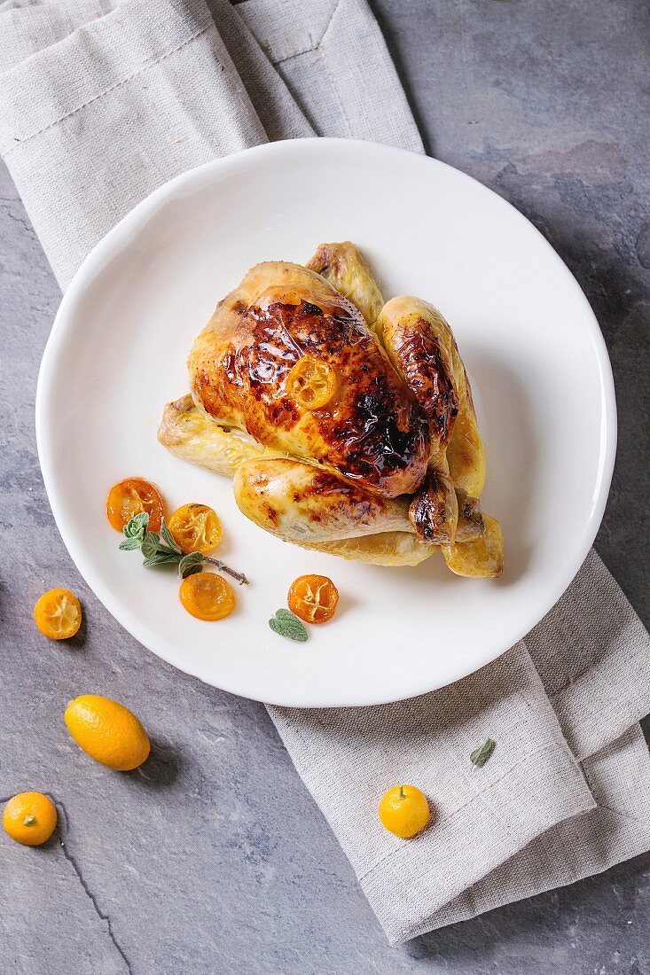 Whole roasted mini chicken cooking with caramelized kumquats served with fresh citrus fruits