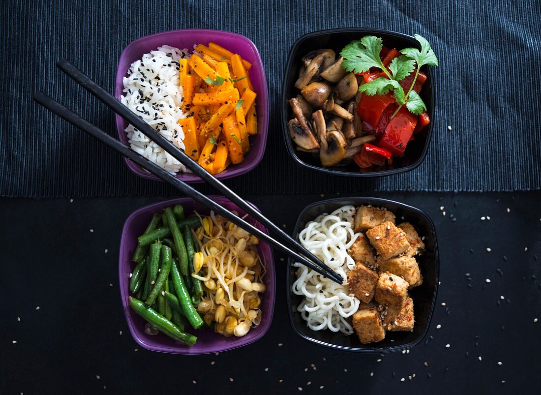 Vier Schalen mit Reis, gebratenen Karotten, Champignons, Paprika, Bohnen, Mungobohnen, Mie-Nudeln und Tofu (vegan)