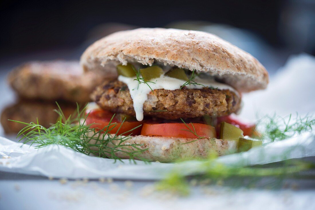 A burger with a millet fritter, tomato, and a dill and cucumber sauce (Vegan)