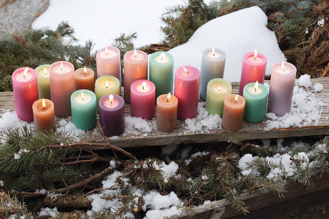 Colourful pillar candles on weathered wooden board amongst snow