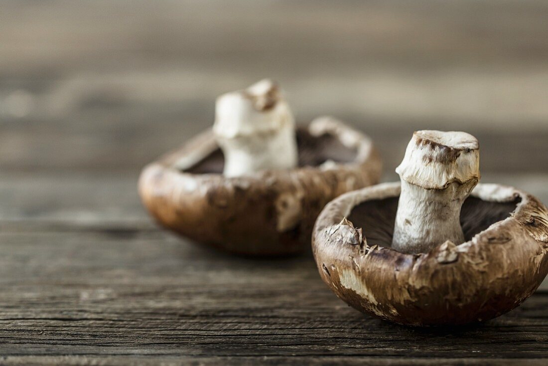 Two portobello mushrooms on a wooden surface