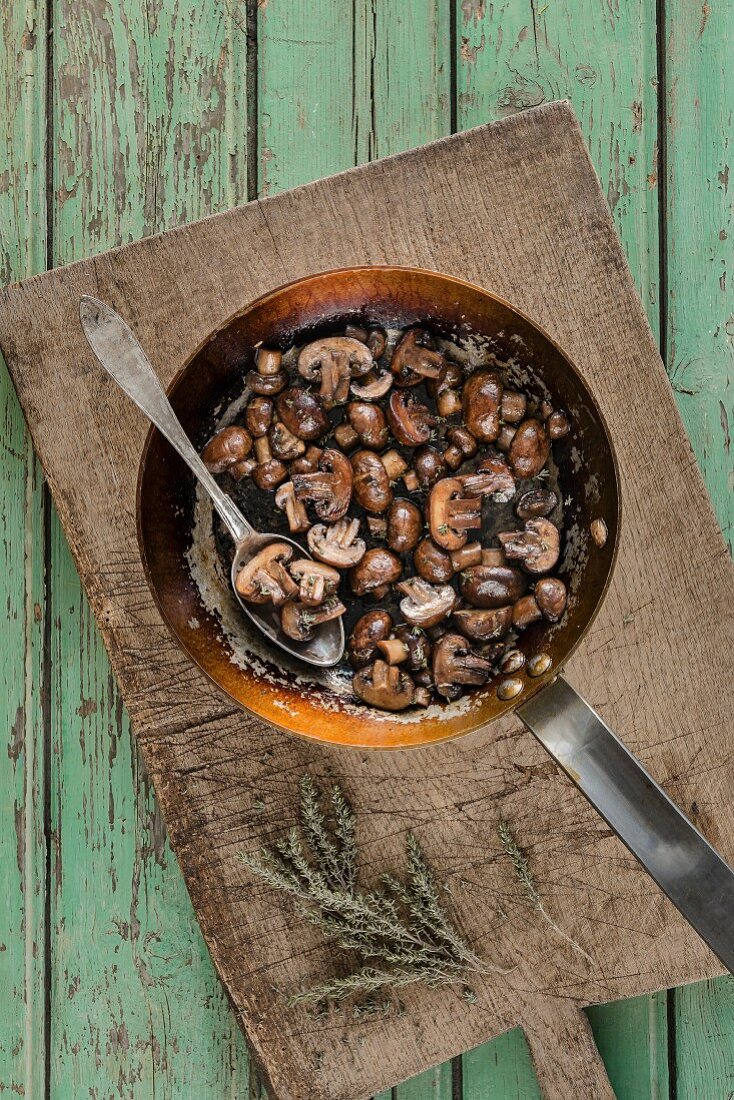 Brown mushrooms glazed in butter marsala wine and thyme in a rustic frying pan with spoon on a wooden chopping board