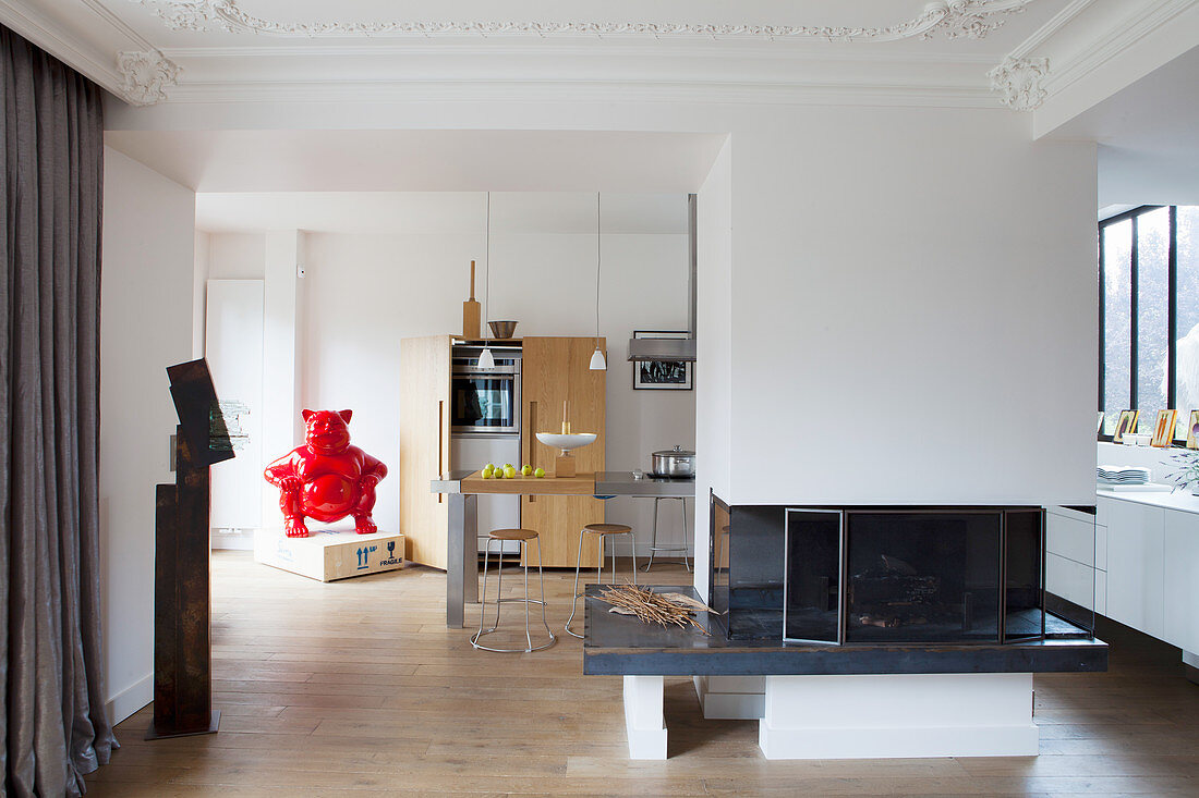 Open fireplace used as partition between living room and modern kitchen in period apartment with stucco elements