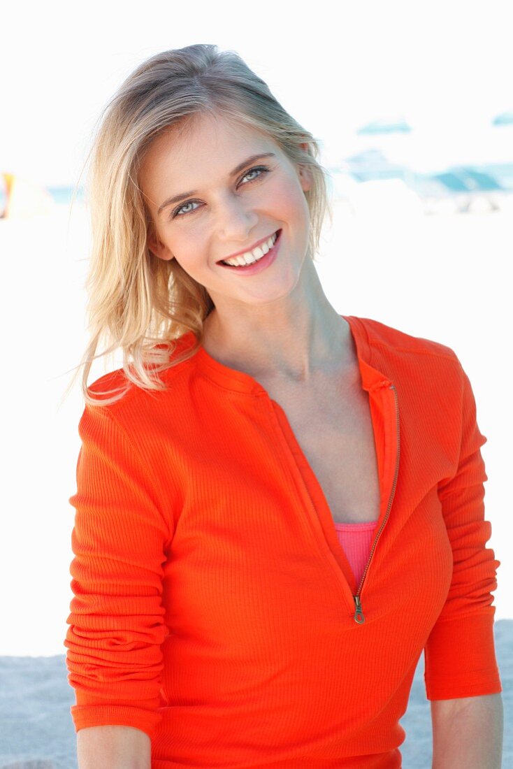 A blonde woman wearing an orange long-sleeved top with zip