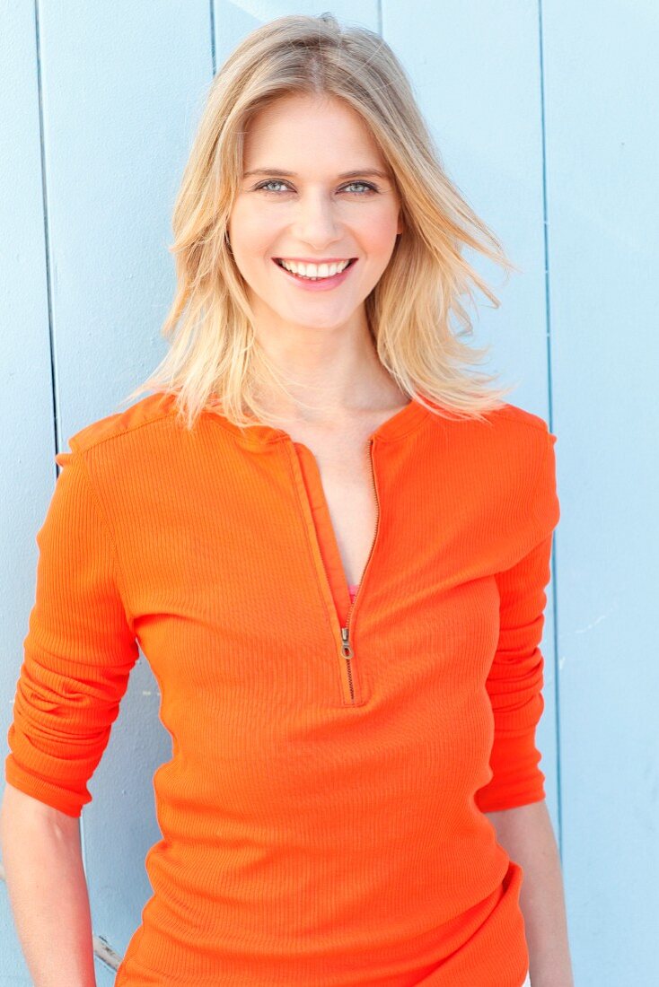 A blonde woman wearing an orange long-sleeved top with zip