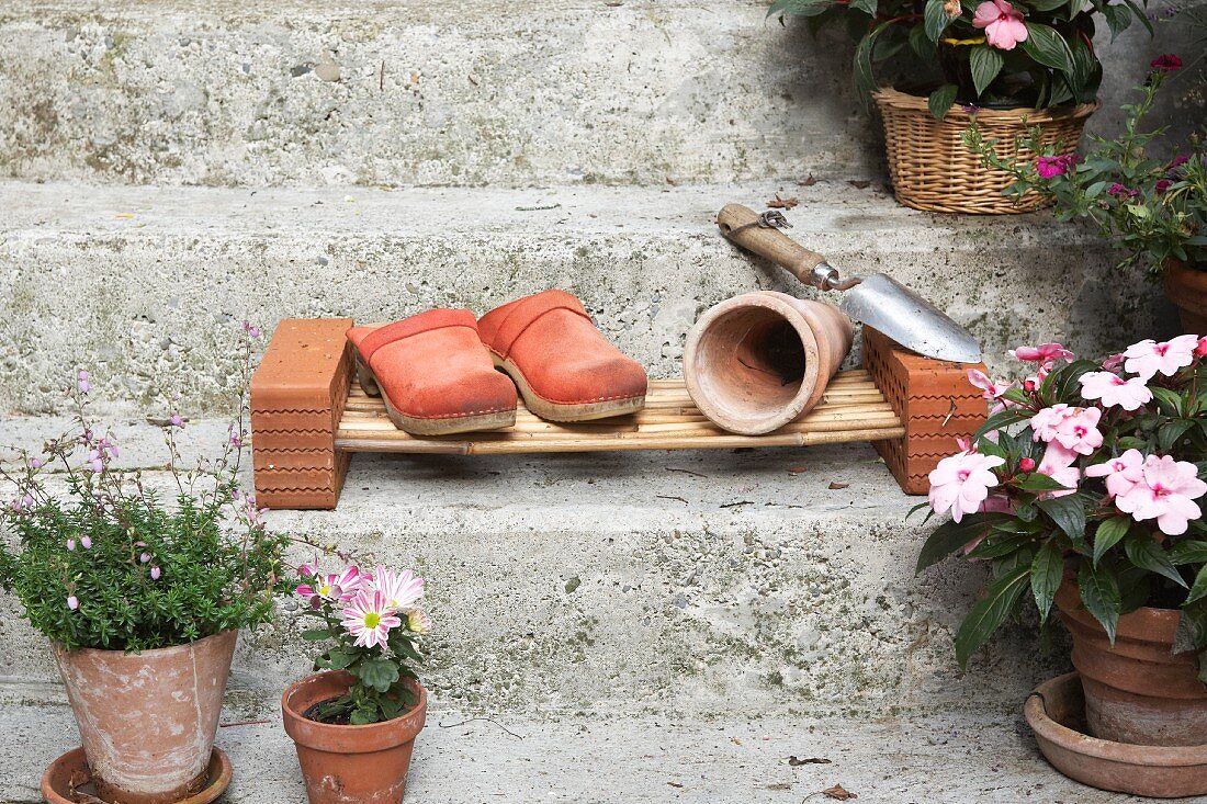 Gartenschuhe und Pflanzentöpfe auf DIY-Schilfpodest auf Steintreppe