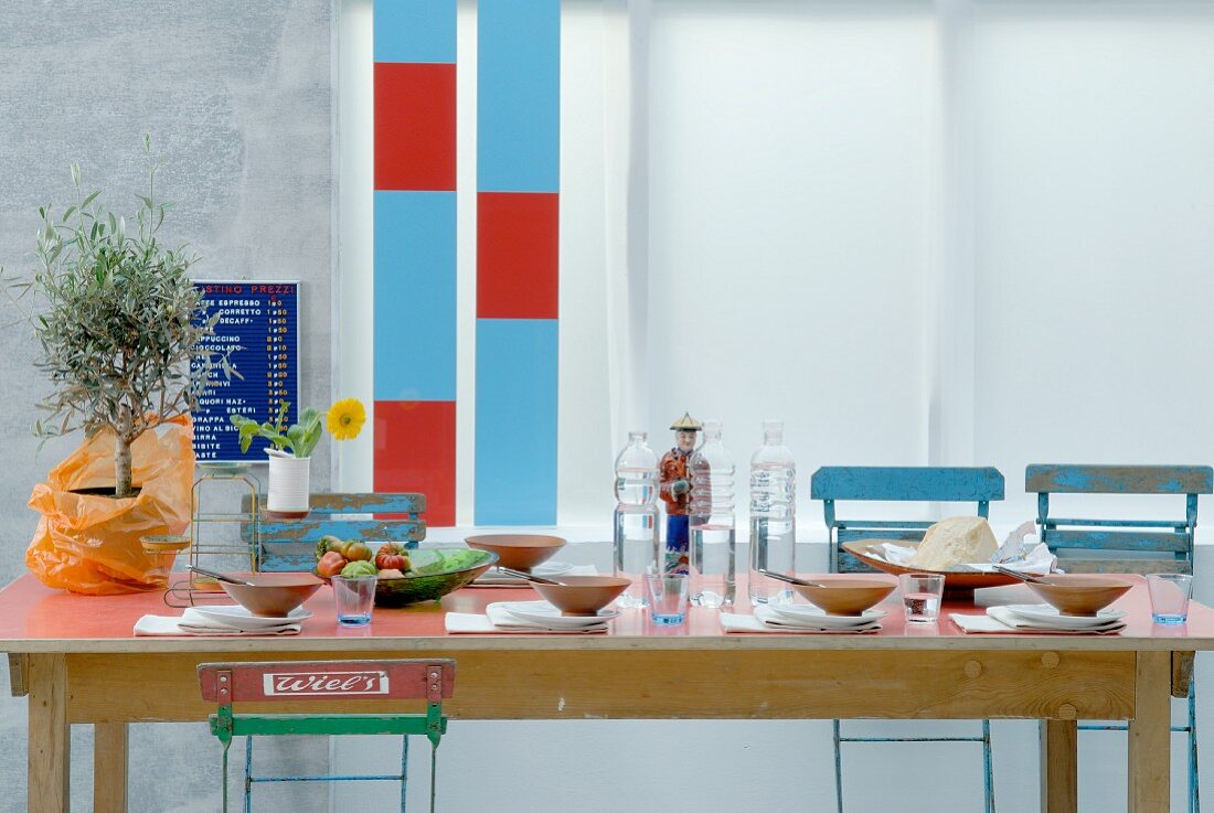 Mahogany bowls, glass bottles. ceramic ornament and potted tree on Mediterranean table surrounded by garden chairs