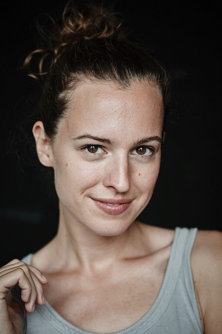 A brunette woman with her hair in a bun, wearing a grey vest top