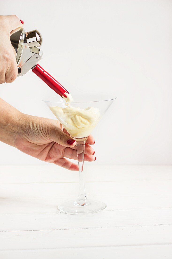 A whipped cream dispenser and cream in a glass