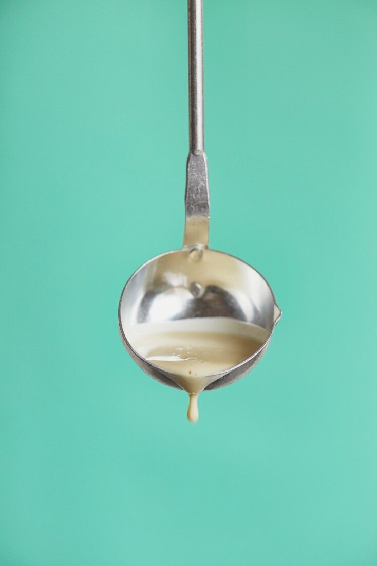 Pancake batter in a ladle in front of a turquoise background