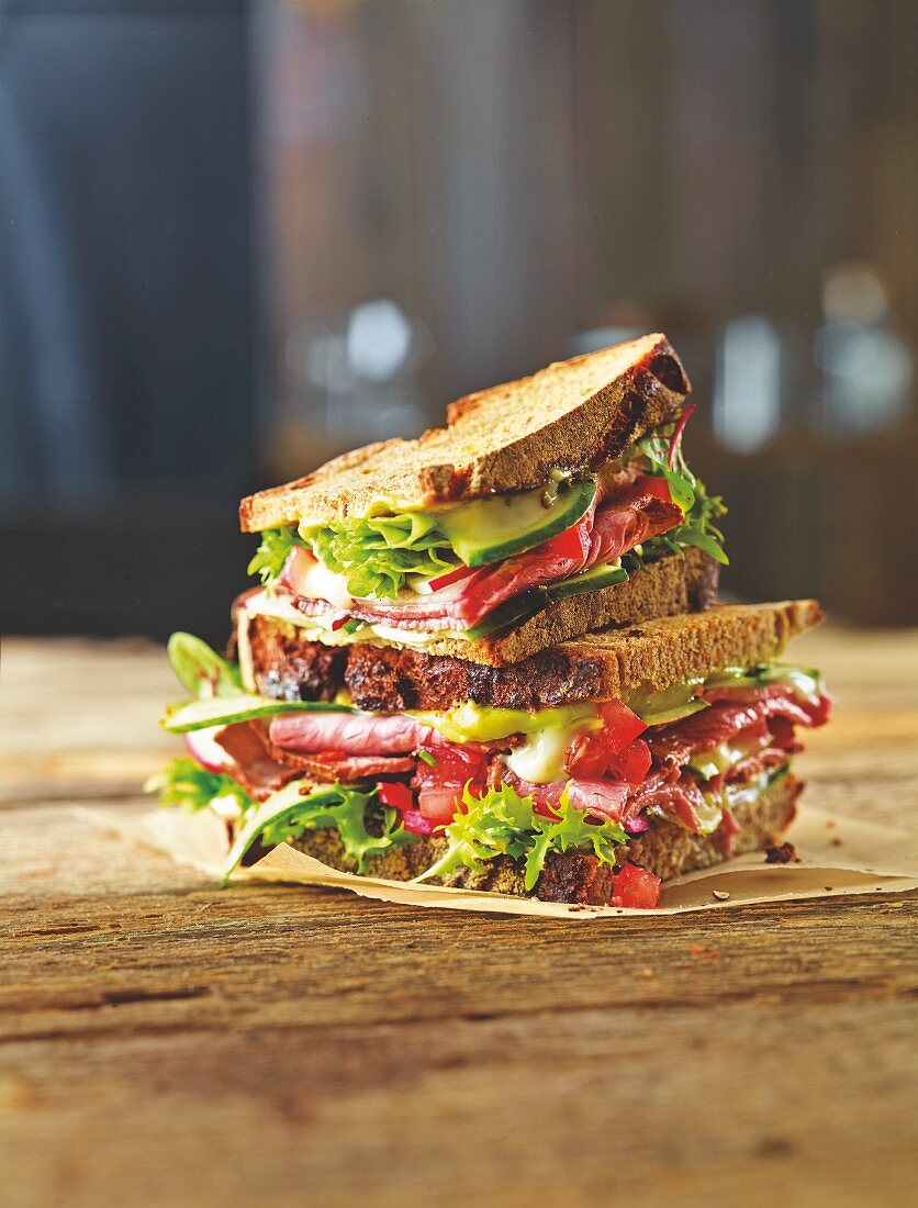 A roast beef sandwich with cucumber, tomato and guacamole