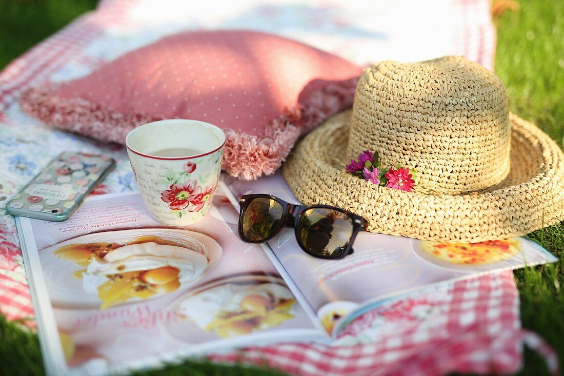 Picknickdecke auf der Wiese mit Kaffee, Strohhut und Zeitschrift
