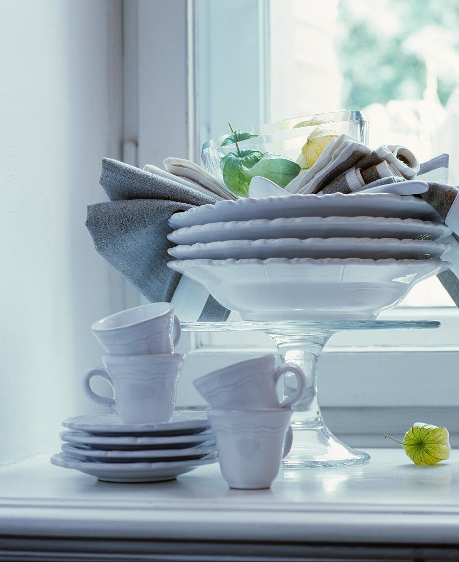 Tellerstapel auf Tortenplatte und weisses Kaffeegeschirr vor Fenster