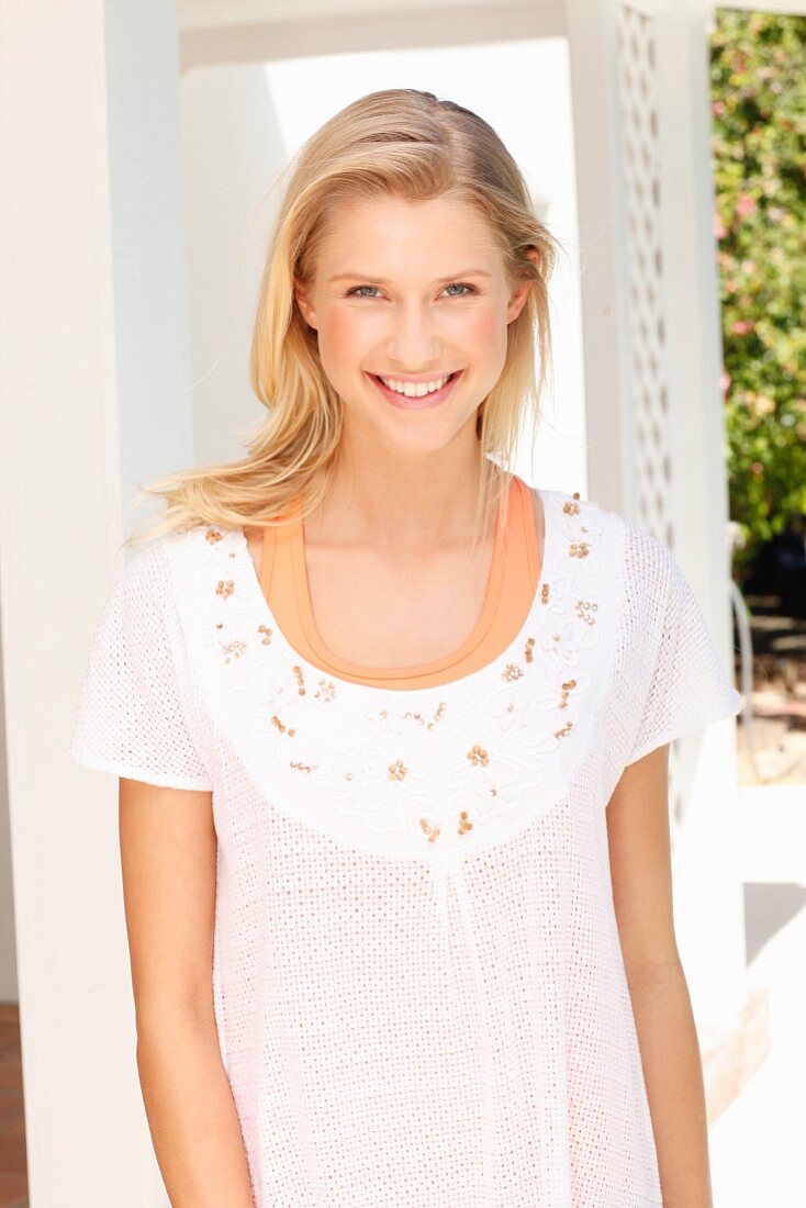 A blonde woman wearing an orange vest and an embroidered white mesh top