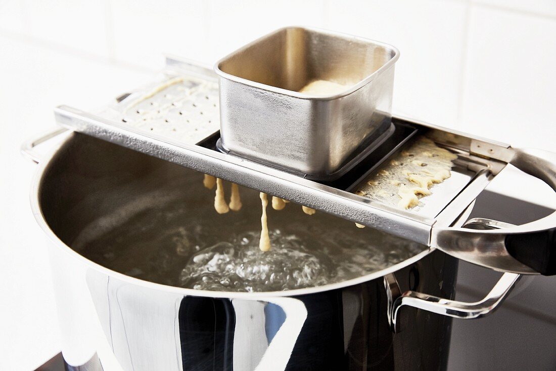 Fresh spaetzle being pressed through a spaetzle plane into boiling water