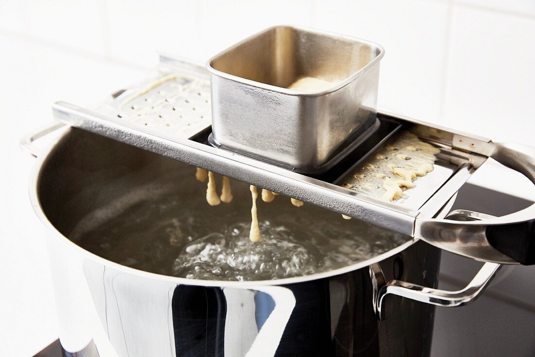 Frische Spätzle mit Spätzlehobel in kochendes Wasser hobeln