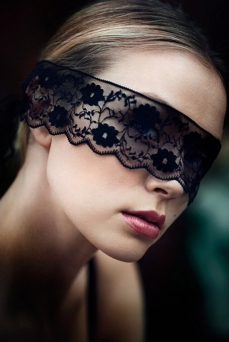 A young blonde woman wearing a black lace blindfold